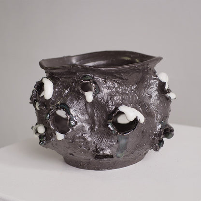 A dark charcoal gray textured ceramic pot with irregular organic protrusions and white accents, photographed on a plain light gray background.