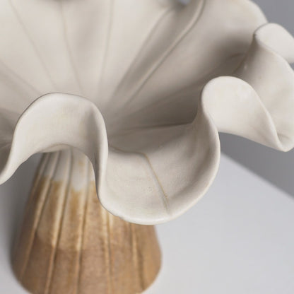 Close-up of a ceramic flower vase with ruffled petals in warm off-white and a fluted base in beige and light brown tones.