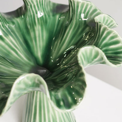 A close-up of a glossy green ceramic flower-shaped vase with ruffled petals and vertical ribbed detailing, shown on a light neutral background.