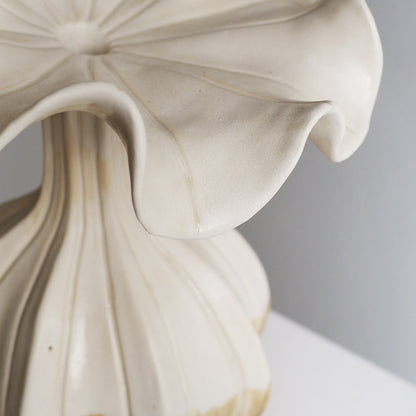 Close-up detail of a cream-colored ceramic vase with a sculpted, petal-like flared top and ribbed base, set against a neutral gray background.