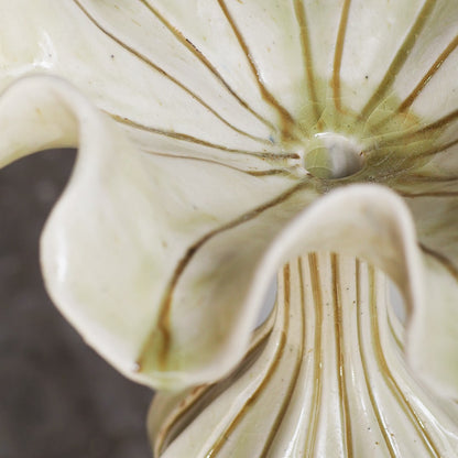 Close-up of a glossy ceramic lily flower vase with cream-colored petals and delicate brown veining, showing the ribbed stem and center hole.